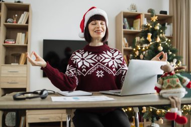 Kadının yoga egzersizi yaparken elinde aletler ve Noel ağacı eviyle süslenmiş kağıtlarla masada oturması ön planda. Noel Baba şapkalı beyaz kadın işten sonra gözleri kapalı dinleniyor..