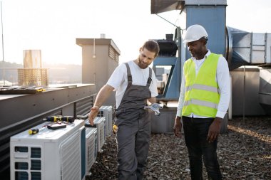 Fabrikada konuşurken ayakta dikilen ve birbirlerine bakan ciddi zanaatkarlar. Klimaları tamir eden ve açık havada sorunları tartışan çok kültürlü meslektaşlarım var..