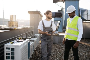 Fabrikada konuşurken ayakta dikilen ve birbirlerine bakan ciddi zanaatkarlar. Klimaları tamir eden ve açık havada sorunları tartışan çok kültürlü meslektaşlarım var..