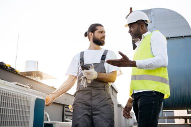 Beyaz sakallı inşaat ayakta duruyor ve klima için ölçüm cihazı kullanırken afro meslektaşı dışarıda pozitif sonuç doğruluyor. Onarım ve aygıt arızası kavramı.