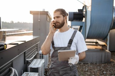 Telsiz cep telefonuyla konuşurken saç örgülü tabletli ciddi bir fabrika işçisi. Beyaz tenli nitelikli adam fabrikanın çatısındaki cihazlarla ilgili sorunları çözüyor.
