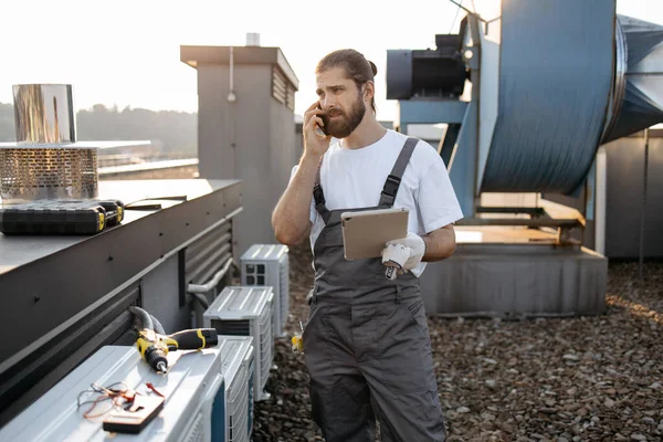 Telsiz cep telefonuyla konuşurken saç örgülü tabletli ciddi bir fabrika işçisi. Beyaz tenli nitelikli adam fabrikanın çatısındaki cihazlarla ilgili sorunları çözüyor.
