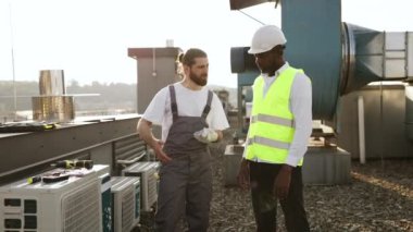 Fabrikada konuşurken ayakta dikilen ve birbirlerine bakan ciddi zanaatkarlar. Klimaları tamir eden ve açık havada sorunları tartışan çok kültürlü meslektaşlarım var..