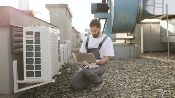 忙碌的工厂工人穿着制服蹲着 在露天平台上使用无线笔记本电脑 白胡子男子为空调提供服务 并在工厂的互联网上查看相关信息 — 图库视频影像