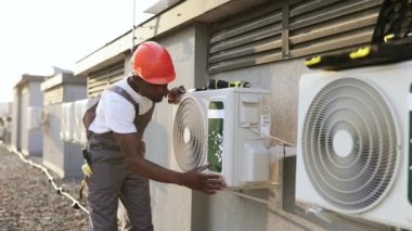 Turuncu şapkalı Afro-Amerikan fabrika işçisi dışarıda duvara bağlanmış klimayı kontrol ederken el ele tutuşuyor. El işi ve ekipman kurulumu kavramı.