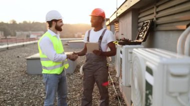 Modern dijital tabletle kontrat yaptıktan sonra el sıkışan yakışıklı çok ırklı zanaatkârların portresi. Açık terasta klimanın yanında duran iki teknisyen..
