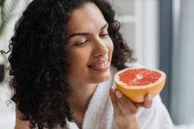 Banyodan sonra sağlıklı bir kadın yatak odasında dinlenirken taze narenciye aromasının tadını çıkarıyor. Büyüleyici yetişkin insan kaliteli güzellik hayatı için C vitamini greyfurt kullanıyor..