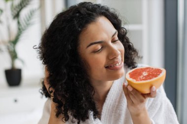 Banyodan sonra sağlıklı bir kadın yatak odasında dinlenirken taze narenciye aromasının tadını çıkarıyor. Büyüleyici yetişkin insan kaliteli güzellik hayatı için C vitamini greyfurt kullanıyor..