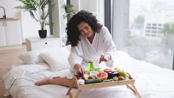 매력적인 아프리카 여성은 사과를 방에서 부드러운 침대에 트레이 테이블에 화장품 — 비디오