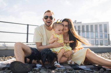 Neşeli yetişkin baba kucağında küçük kızı ve köpeği tutarken gülümseyen ve karısının yanında oturan. Kafkas tarzı eşlerin birlikte eğlenmesi ve çocukların binanın çatısında mutlu bir çocukluk geçirmesi.