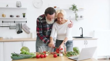Ellerinde bıçakla cam kaseye parçaları koyarken biber kesen pozitif emekli çift. Eski aile boş zamanlarını modern mutfakta sağlıklı salata yaparak geçirir..