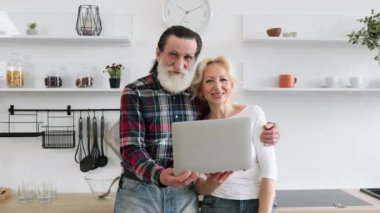 Lezzetli kahvaltı için internetten alışveriş yapan mutlu yaşlı çiftin portresi. Gri saçlı karı koca salata tarifi arıyorlar. Mutfakta dizüstü bilgisayar kullanıyorlar.