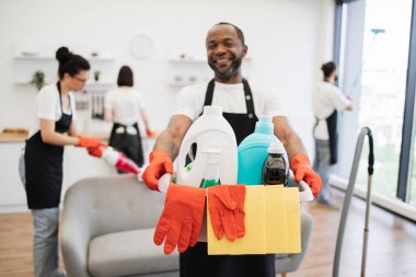 Afrika kökenli Amerikalı genç bir adamın ellerinde deterjanlar ile yıkanacak kovaya odaklanın profesyonel temizlik işçisi parlak mutfak stüdyosu arka planı, kopyalama alanı.