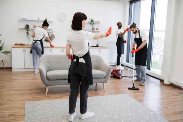Professional housekeeper services company team working at customer house washing dishes, kitchen cleaning. Female boss of company distributes tasks to employees and points to cleaning locations.