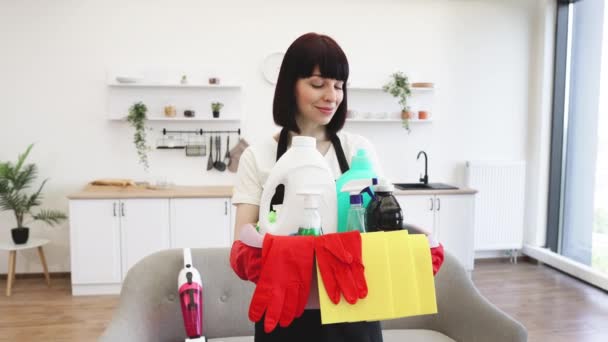 明るいキッチンスタジオの背景に洗剤で洗濯するためのバケツを持っている若い白人女性のプロのクリーニングワーカーのフロントビュー コピースペース — ストック動画
