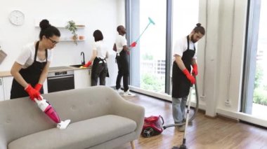 Çok ırklı iş arkadaşlarının yanında modern bir dairede panoramik pencere camlarını paspasla temizleyen Afro-Amerikalı pozitif işçilere odaklan.