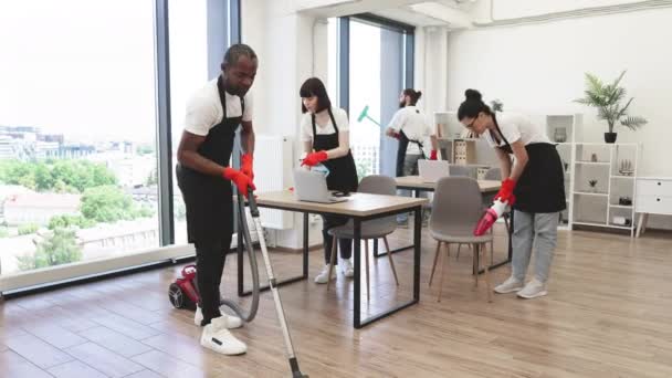 多文化的清洁工团队在宽敞 现代的办公室里擦桌子和小玩意 非裔美国人使用真空吸尘器清洁地面 显示大拇指以上的污垢 — 图库视频影像