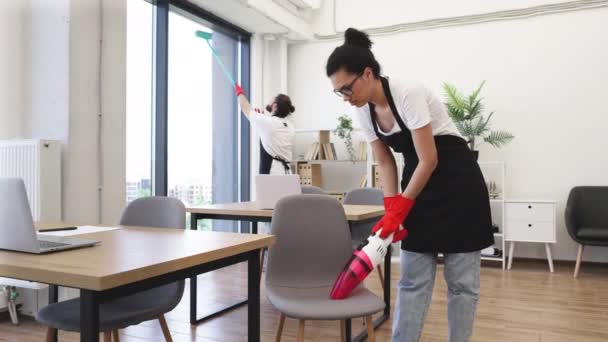 多种族的年轻女性清洁吸尘椅与便携式无绳吸尘器 在明亮宽敞的现代化办公室里为公司清洁的多文化员工感到高兴 — 图库视频影像