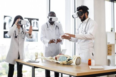 Laboratuvarda insan iskeleti anatomisi üzerinde çalışan çok ırklı genç doktorlar, biyoendeciler, sanal gerçeklik ekipmanlı bilim adamları ve VR gözlükleri var..