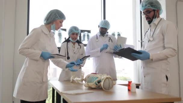 印度女医学教师向大学生或年轻医生教授解剖学 阿拉伯和非洲男人 白人女人站在桌旁 用人体器官做人体骨骼模型 — 图库视频影像