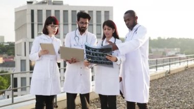 Klinik yakınlarındaki çok ırklı meslektaşlarına yapılan testlerin sonuçlarını gösteren dizüstü bilgisayar kullanan genç bir Arap doktor. Ortaklarla deneyimli ve bilgili tıbbi uzman paylaşımı.