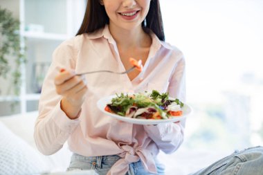 Ellerinizi salata ve çatalla kapayın ve hafta sonları kahvaltıdan zevk alan beyaz kadın sebzeleriyle birlikte. Güzel kadın evde yatakta dinleniyor, kahvaltı yaparken dizüstü bilgisayar kullanıyor..