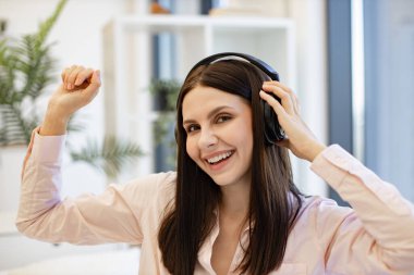 Kulaklıklı mutlu bayan rahat bir yatakta oturuyor ve hafta sonları dinlenme müziğinin keyfini çıkarıyor. Evdeki favori müziği dinleyen modern aletler kullanan mutlu bir kadının portresi..