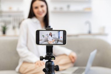 Kafkasyalı kadın etkili video kaydını modern akıllı telefondan dizüstü bilgisayarla koltukta otururken yapıyor. Mutlu genç kadın başarısını internetteki abonelerle paylaşıyor.