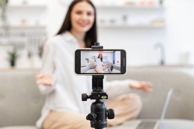 Çevrimiçi eğitim için tripodlu modern akıllı telefon kullanmayı talep ediyor. Beyaz saçlı, esmer bir kadın sosyal ağda canlı yayında modern laptoptan bilgi okuyor..