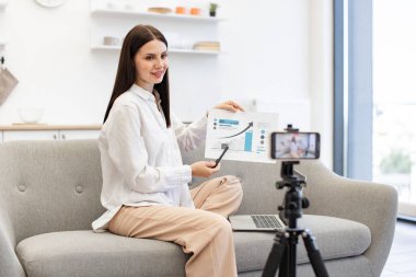 Hevesli genç beyaz kadın okutman cep telefonuyla video bağlantısıyla finansal okuryazarlık öğretiyor. Zeki profesör canlı yayın sırasında öğrencilere para birimi büyüme grafiği gösteriyor.