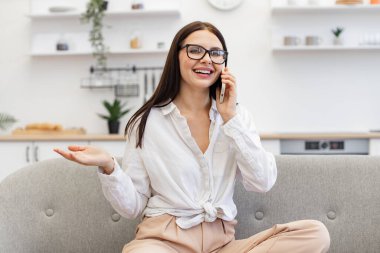 Rahat koltukta otururken iş arkadaşlarıyla sohbet eden gündelik kıyafetli hoş bir kadın. Modern akıllı telefonlarda konuşurken, evde otururken, beyaz kadın hareketlerine olumlu yaklaşıyorum..