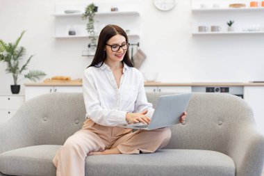 Rahat evdeki serbest çalışma sırasında yeni bir fikirden esinlenen heyecanlı beyaz kadın hissi. Mutlu esmer iş kadını rahat koltukta oturuyor ve taşınabilir laptop kullanıyor..