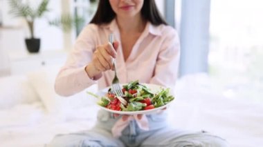 Salata ve çatallı tabağa odaklan. Kadın ellerinde. Hafif, modern, rahat yatak odasında kahvaltıdan zevk alıyor. Kafkasyalı kadın rahat bir yatakta oturmuş sağlıklı salata yiyor..