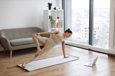 Vasisthasana egzersizini kullanarak genel esneklik kazandıran etkin ve zayıf bir bayan. Dar spor kıyafetleri içindeki olgun atletik kadın yoga antrenmanı sırasında zemine minder serpiştiriyor..