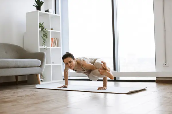 Strong attractive woman standing on hands and keeping legs up during power yoga indoors. Active brunette in sport outfit practicing various position body endurance and balance while training.