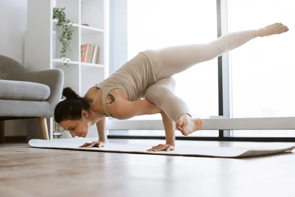 Active brunette in sport outfit practicing various position body endurance and balance while training. Strong attractive woman standing on hands and keeping legs up during power yoga indoors.