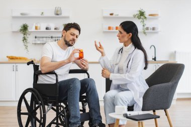 Tıbbi geçmişle ilgili tavsiyeleri dinleyen odaklanmış tekerlekli sandalye kullanıcısı. Kadın doktor, evde, mutfakta engelli bir hastaya uzman muayenesi ve ilaç veriyor..