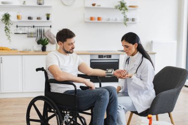 Tekerlekli sandalyedeki yetişkin adam sağlıklı bir hayat sürmenin gerekliliğini anlatıyor. Çekici kardiyolog engelli hastaya evde hipertansiyon olmasının tüm nedenlerini anlatıyor..