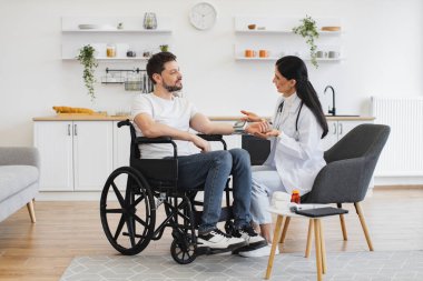 Engelli kadın doktor ve hasta modern mutfakta teşhis ve sağlık kontrolünden bahsediyorlar. Elektronik ekranı olan özenli bir adam kadın doktoru dikkatle dinliyor..