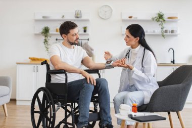 Elektronik ekranı olan özenli bir adam kadın doktoru dikkatle dinliyor. Engelli kadın doktor ve hasta modern mutfakta teşhis ve sağlık kontrolünden bahsediyorlar..