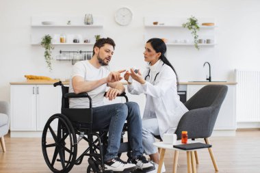 Kadın doktor termometreyi evde sakat bir hastayla erkeğinin vücut ısısını ölçmek için hazır tutuyor. Vücut ısısı ölçümü. Kızılötesi lazer temassız termometre.