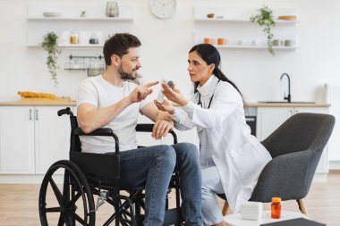 Hoş esmer kadın doktor portresi. Evde özürlü erkek hastasını ziyaret ediyor. Dijital kızılötesi termometredeki vücut ısısının ölçümünü gösteriyor..