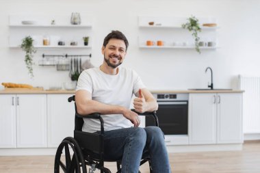 Engelli beyaz bir adamın portresi. Geniş yemek odasında poz veriyor, başparmağını gösteriyor. Olumlu genç yetişkinler evdeki yaralarını iyileştirirken iyimser hissediyorlar..