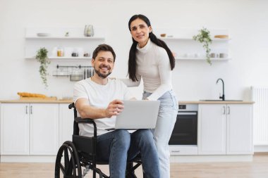 Tekerlekli sandalyede dizlerinin üzerinde dizlerinin üzerinde duran mutlu beyaz adam portresi açık uzay mutfağının ortasında güzel karısına iş sonuçlarını gösteriyor..