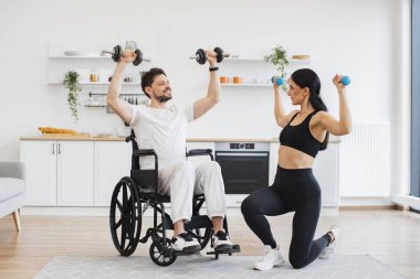 Spor giyim sektöründe milenyum fizyoterapisti tekerlekli sandalyedeki engelli bir adamın halterlerle antrenman yapmasına ve evdeki sakatlığından kurtulmasına yardım ediyor. Genç erkek hasta için rehabilitasyon.