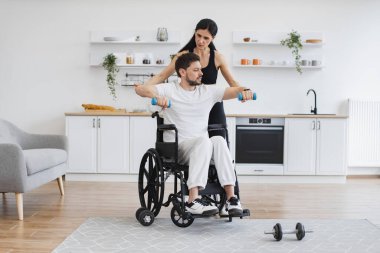Hemşire ya da eş, rehabilitasyonda kas gücü sağlamak için tekerlekli sandalyedeki olgun bir adamın kollarını kaldırmasına yardım ediyor. Fizyoterapi sağlık hizmetleri, tıbbi doktor engelli Kafkas hastalarına danışmanlık.