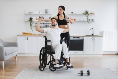 Hemşire ya da eş, rehabilitasyonda kas gücü sağlamak için tekerlekli sandalyedeki olgun bir adamın kollarını kaldırmasına yardım ediyor. Fizyoterapi sağlık hizmetleri, tıbbi doktor engelli Kafkas hastalarına danışmanlık.