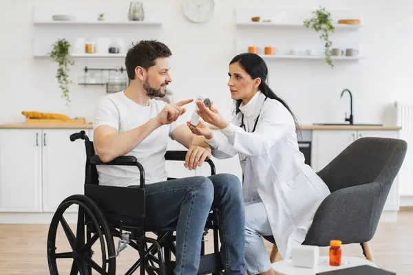 Hoş esmer kadın doktor portresi. Evde özürlü erkek hastasını ziyaret ediyor. Dijital kızılötesi termometredeki vücut ısısının ölçümünü gösteriyor..