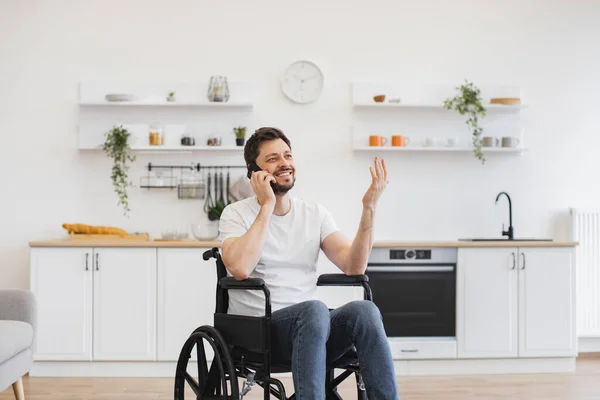 Close up view of bearded male with mobility impairment being involved in phone talk while relaxing in home interior. Confident person discussing after dinner activity with friends outside apartment.