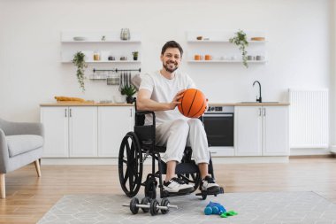 Evde günlük egzersiz yapmadan önce el ele tutuşan hareket sorunu olan beyaz bir yetişkinin tam boy portresi. Tekerlekli sandalyedeki günlük giysiler içinde basketbolcu evde pozitif kalıyor.